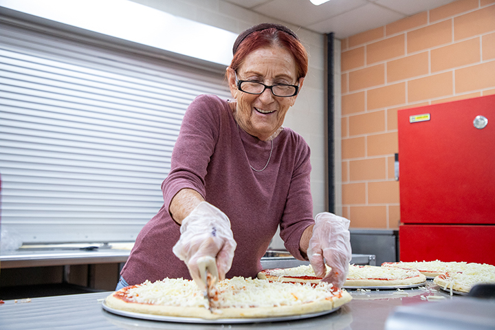 A woman with glasses smiles as she slices a pizza