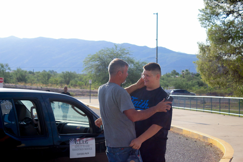 A teen boy hugs his dad by their car on the first day of school